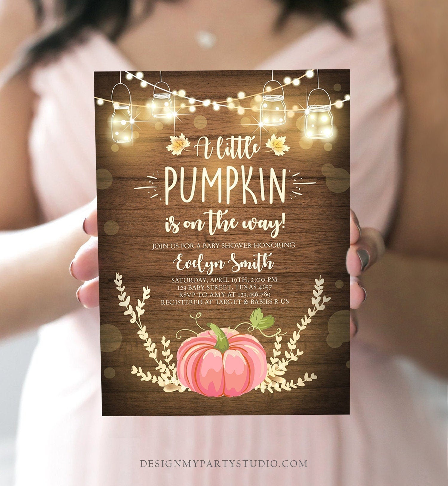 May include: A baby shower invitation with a rustic wood background. The invitation features a pink pumpkin with fall leaves and string lights. The text reads 'A little pumpkin is on the way!' and 'Join us for a baby shower honoring Evelyn Smith'. The invitation also includes the date, time, location, RSVP information, and registry information.