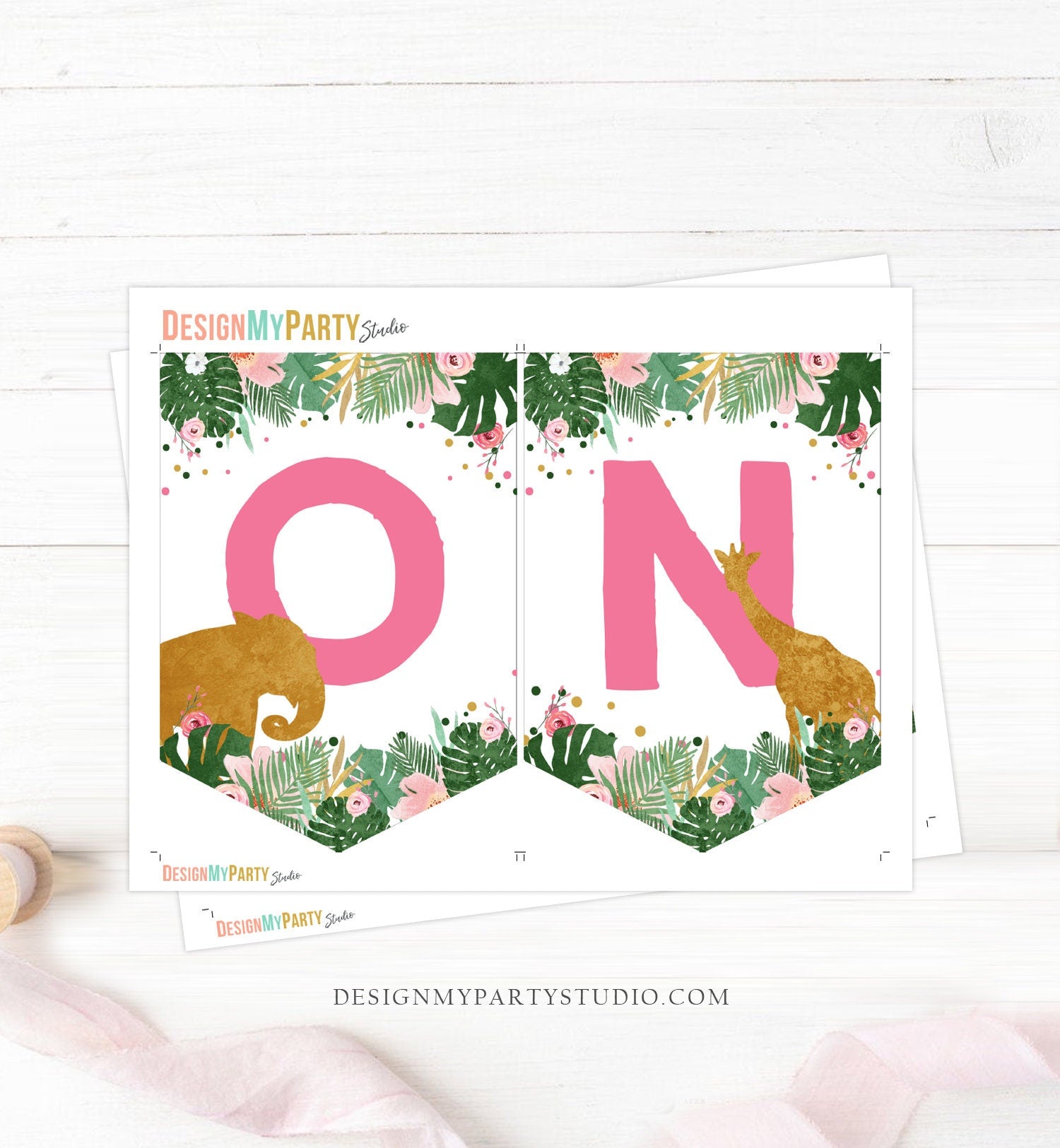 May include: Pink and gold high chair banner with the word &#39;ONE&#39; in pink letters. The banner has a tropical theme with green leaves, pink flowers, and gold glitter. There are also gold animal silhouettes on the banner, including a giraffe, elephant, and lion.
