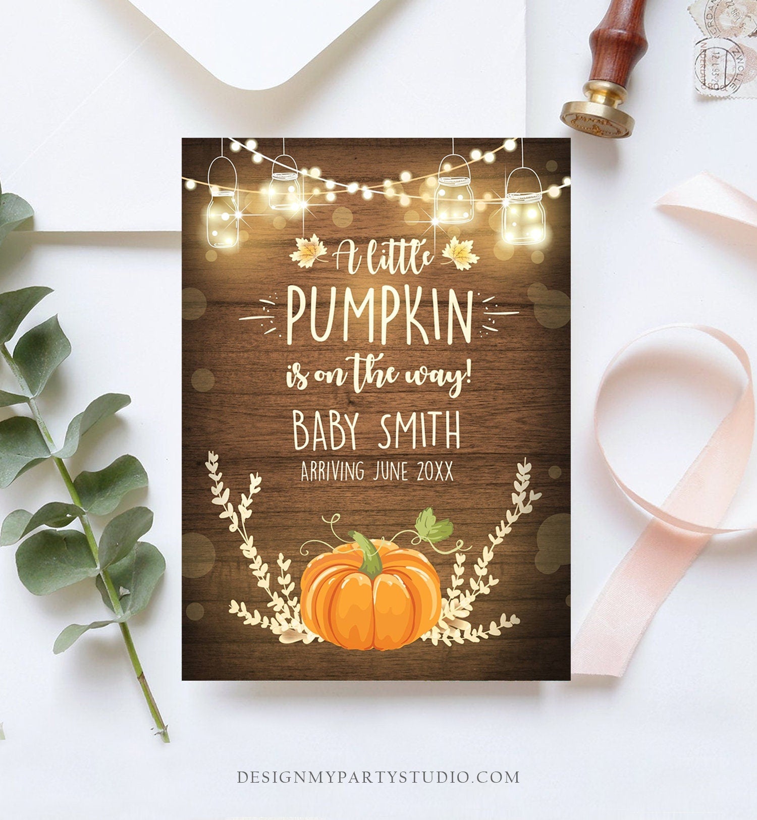 May include: A baby shower invitation with a rustic wood background. The invitation features a pumpkin with a stem and leaves, a string of lights with mason jars, and the text &#39;A little pumpkin is on the way! Baby Smith Arriving June 20XX&#39;.