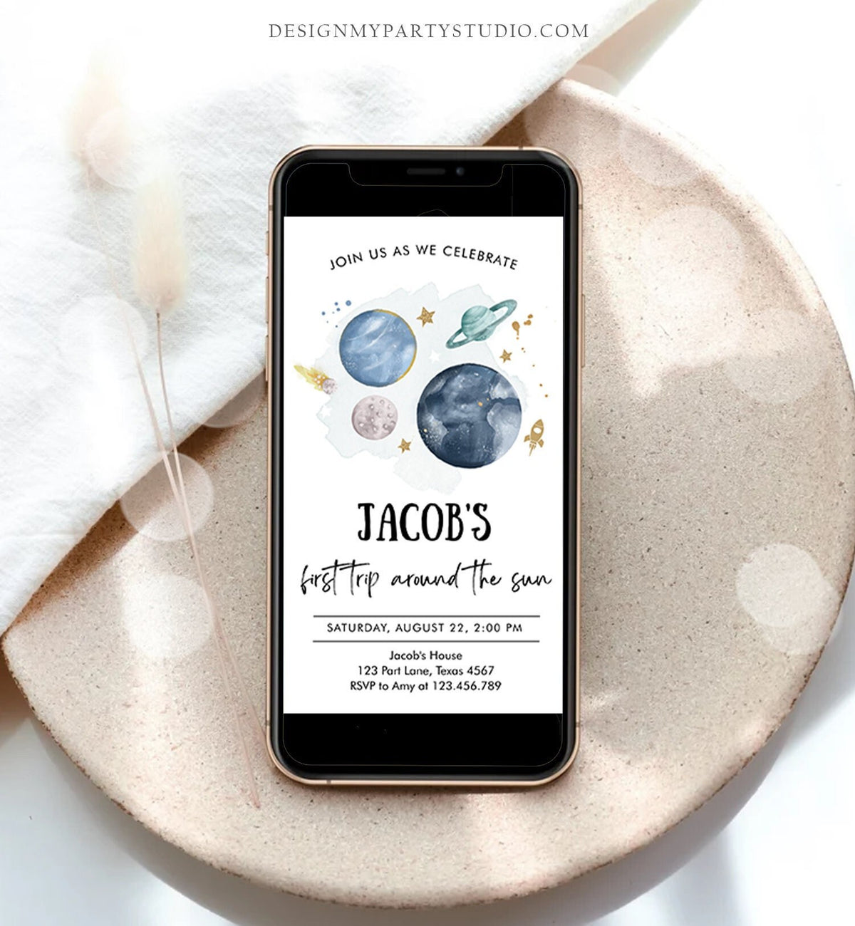 May include: A smartphone mockup with a blue and green space-themed birthday party invitation. The invitation reads &amp;#39;Join us as we celebrate Jacob&amp;#39;s first trip around the sun. Saturday, August 22, 2:00 PM. Jacob&amp;#39;s House, 123 Part Lane, Texas 4567. RSVP to Amy at 123.456.789.&amp;#39;