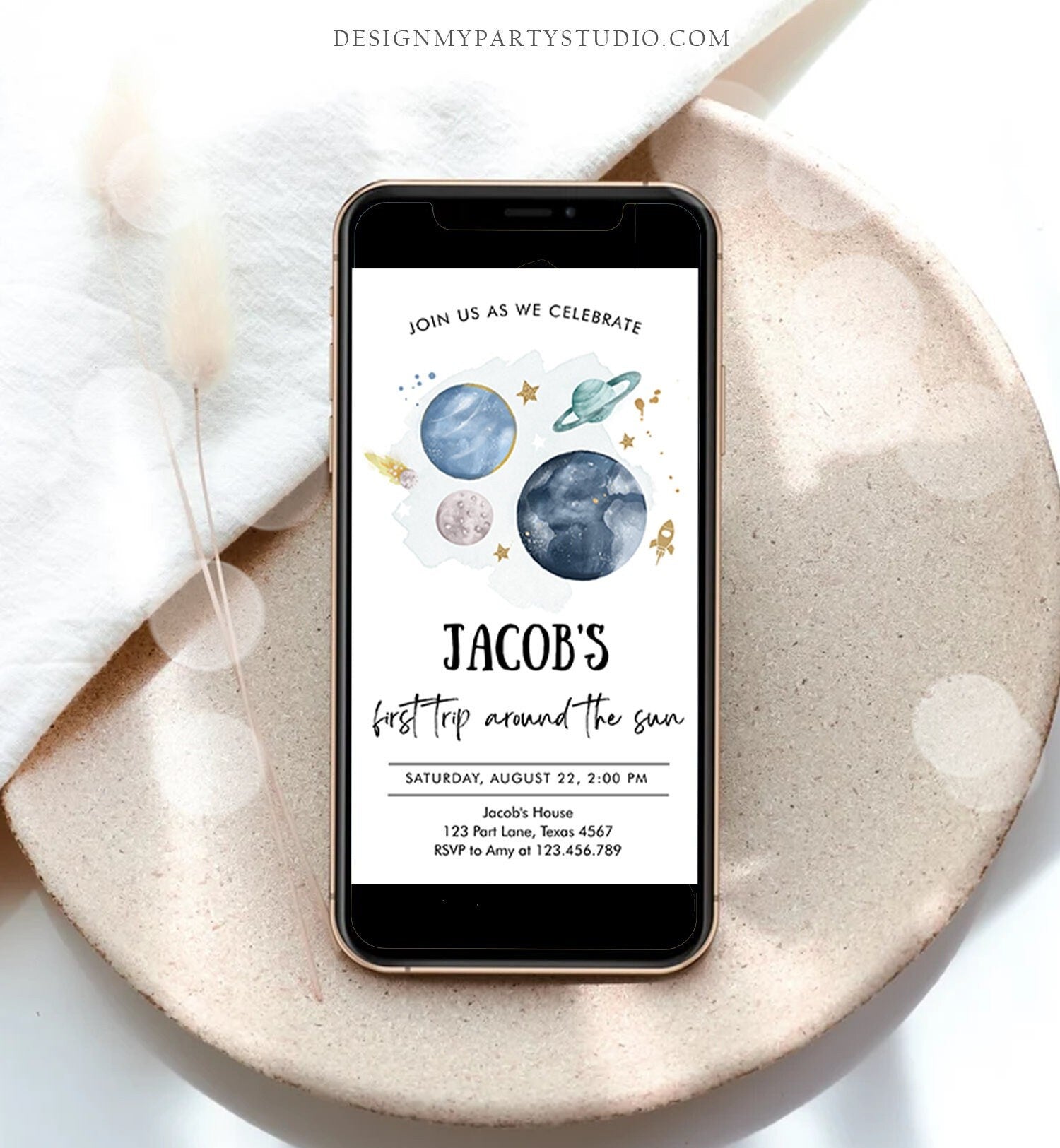 May include: A smartphone mockup with a blue and green space-themed birthday party invitation. The invitation reads 'Join us as we celebrate Jacob's first trip around the sun. Saturday, August 22, 2:00 PM. Jacob's House, 123 Part Lane, Texas 4567. RSVP to Amy at 123.456.789.'