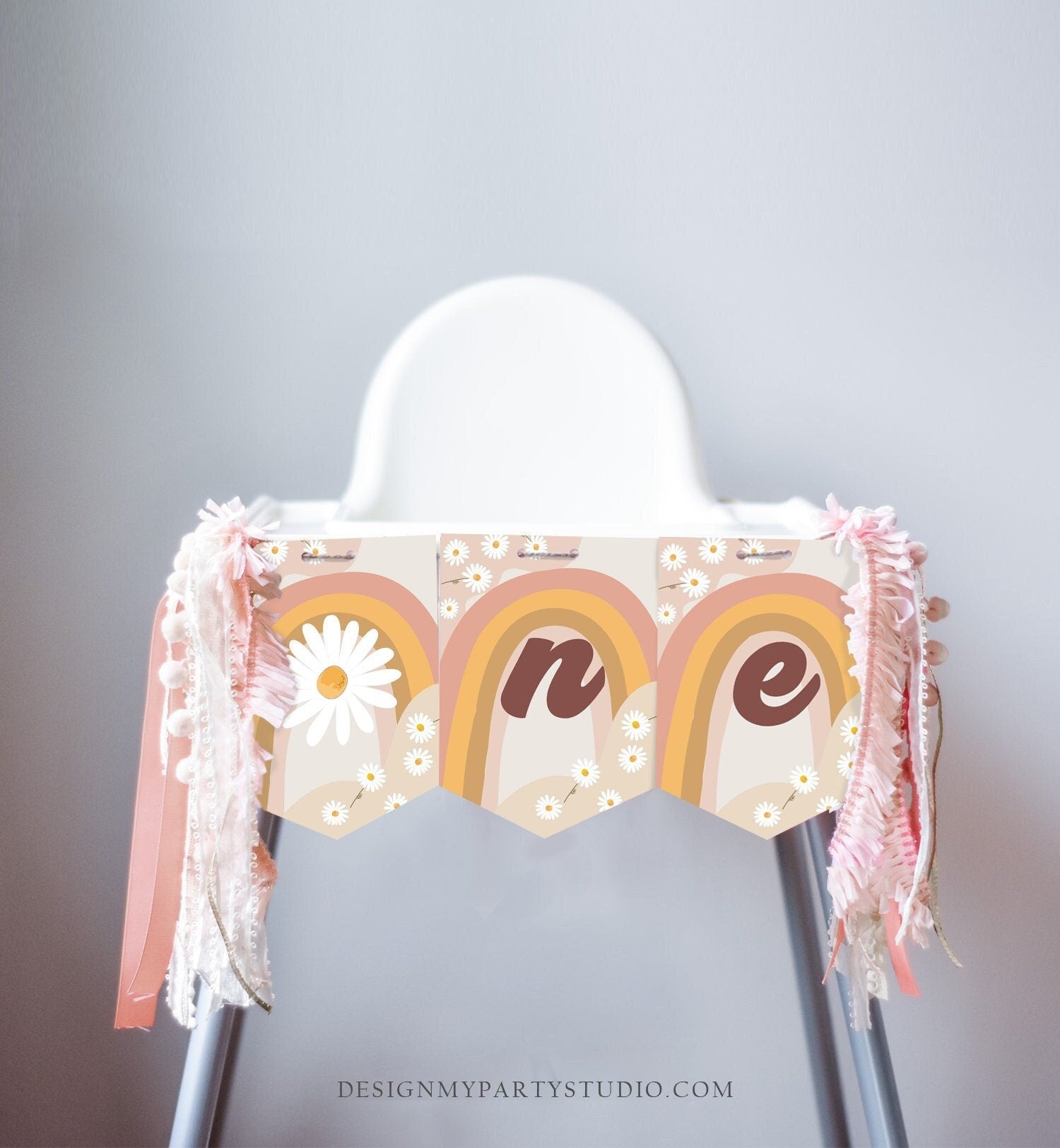 May include: A high chair decorated with a banner that says &#39;one&#39; in brown letters. The banner is made of three pennants with a rainbow and daisy pattern. The pennants are attached to the high chair with pink and white ribbon.