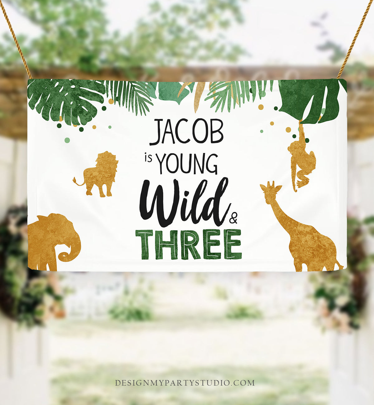 May include: A white banner with green and gold jungle animal silhouettes. The banner reads &amp;#39;Jacob is young wild &amp; three&amp;#39; with the words &amp;#39;wild&amp;#39; and &amp;#39;three&amp;#39; in green and the rest in black. The banner is decorated with green leaves and gold confetti.