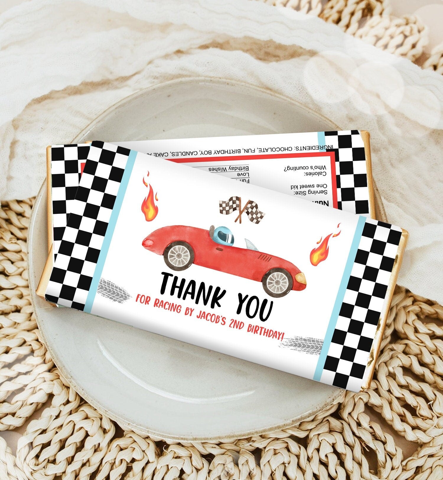 May include: A red race car with checkered flags and flames on a white chocolate bar wrapper. The wrapper has a black and white checkered border. The text on the wrapper reads &#39;Thank You for racing by Jacob&#39;s 2nd birthday!&#39;.