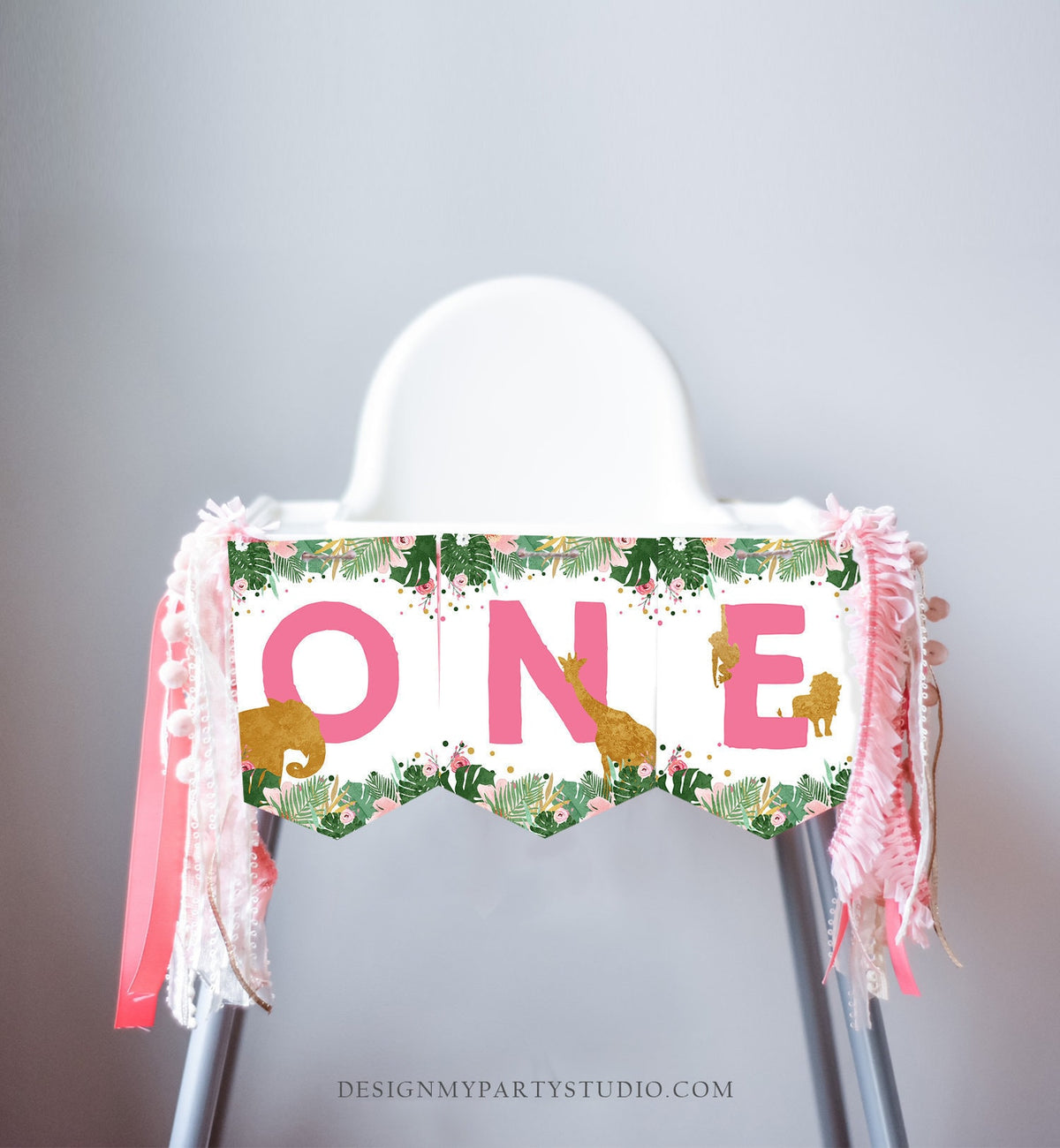 May include: Pink and gold high chair banner with the word &amp;#39;ONE&amp;#39; in pink letters. The banner has a tropical theme with green leaves, pink flowers, and gold glitter. There are also gold animal silhouettes on the banner, including a giraffe, elephant, and lion.