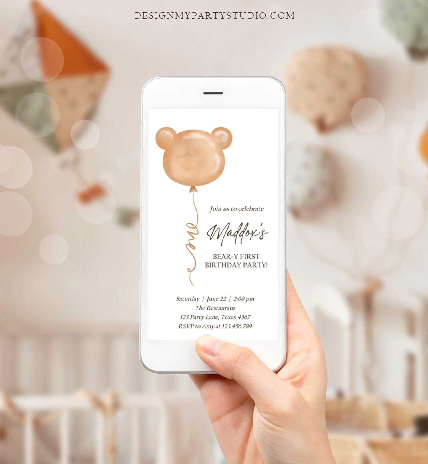 May include: A smartphone displaying a brown bear-themed first birthday party invitation. The invitation has a brown bear balloon with ears, the text &#39;Join us to celebrate Maddox&#39;s BEAR-Y FIRST BIRTHDAY PARTY!&#39; and the details &#39;Saturday June 22 | 2:00 pm The Restaurant 123 Party Lane, Texas 4567 RSVP to Amy at 123.456.789&#39;